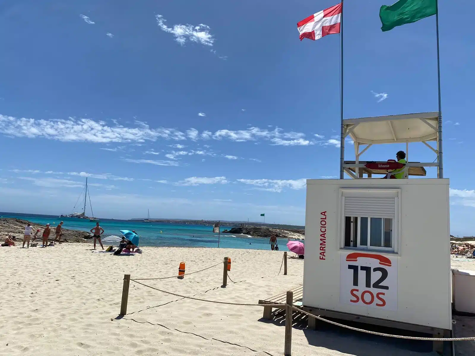Rettungsschwimmerstation am Strand Llevant auf Formentera, mit einem Rettungsschwimmer auf dem Turm, Flaggen und dem Schild 112 SOS